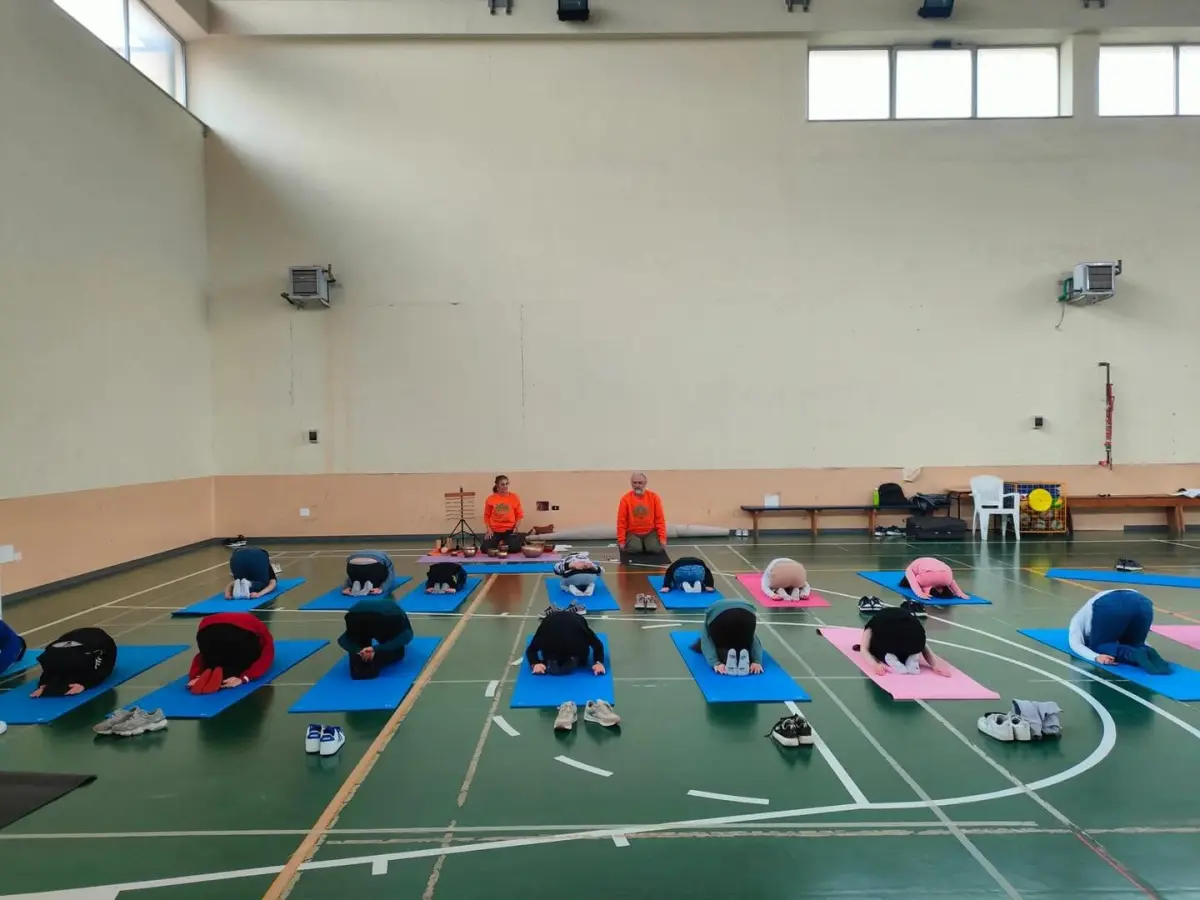 Lezione di yoga per adulti dell'Associazione Dharmonia: i partecipanti in posizione del bambino sui tappetini, con gli istruttori e le campane tibetane sullo sfondo